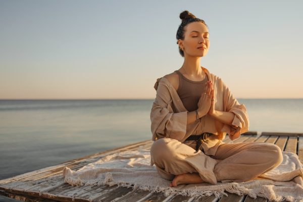 A woman meditating on top of a wooden deck with the sea on the background