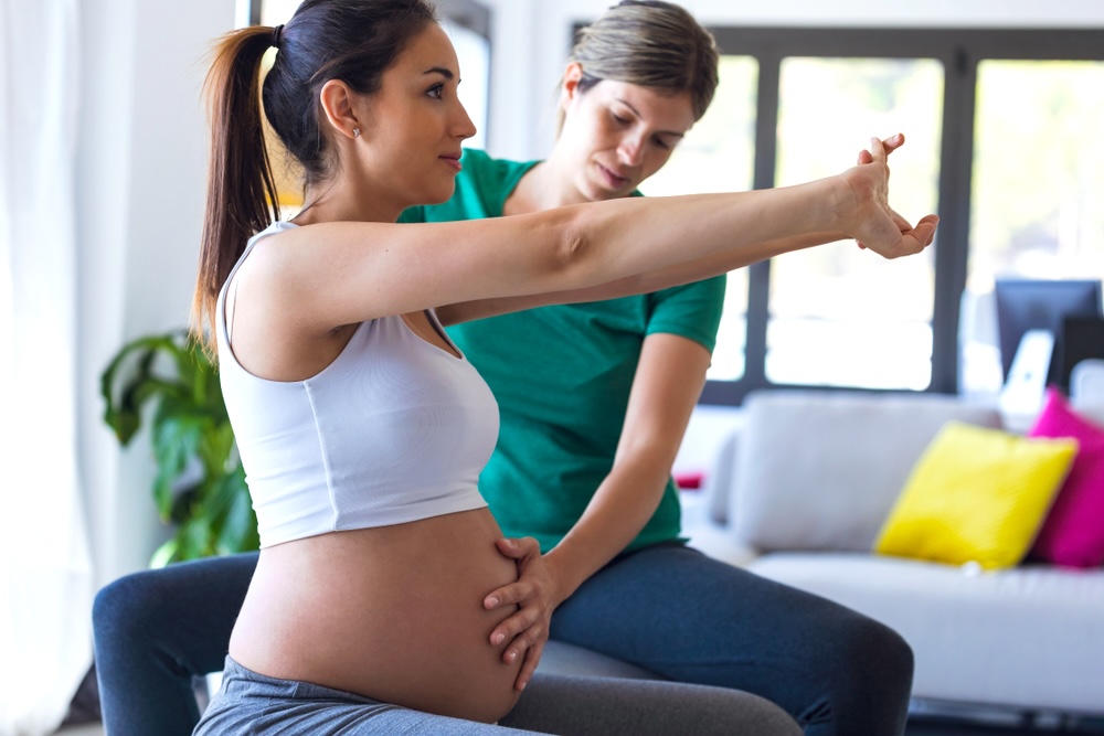 A private yoga instructor guides a pregnant woman while she is stretching