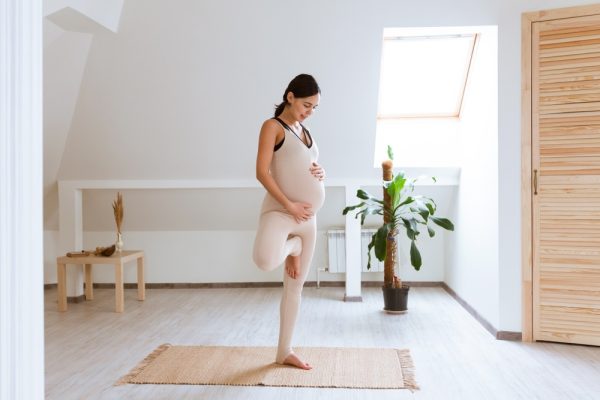 A pregnant woman standing on a yoga mat holding her belly