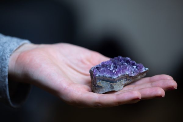 Hand holding an amethyst crystal to activate crown chakra