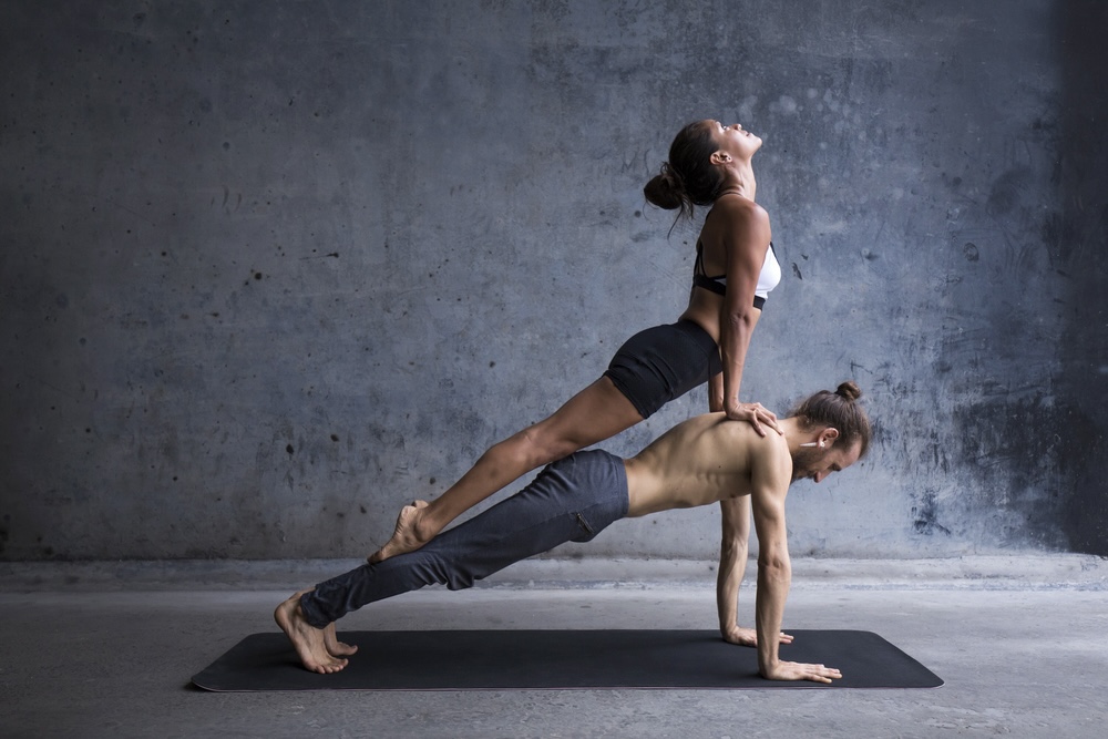Couples practicing a yoga pose with the female partner on the back of her male partner