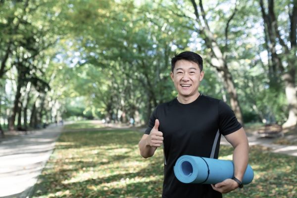 Man in a local park holding a yoga mat after a class