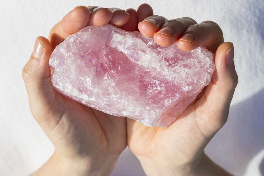 Large rose quartz crystal being held in two palms