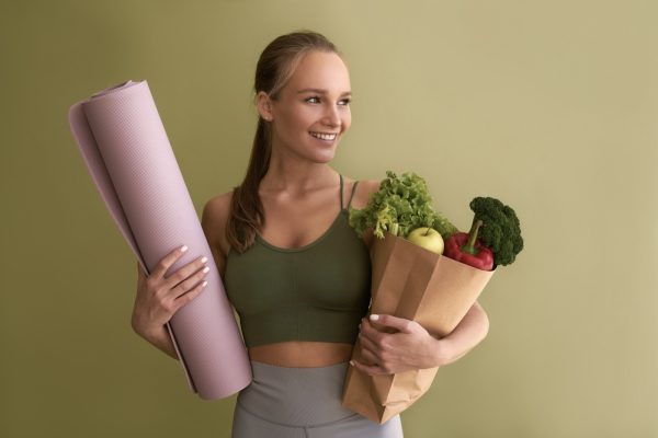 Female yogi holding a yoga mat and healthy fresh groceries