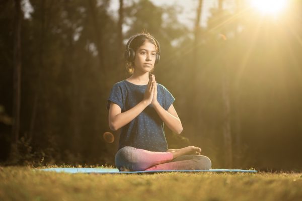 Teen meditating outdoors with headphones listening to affirmations