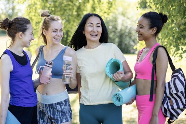 Smiling group of women talking before a yoga class, holding mats and water bottles