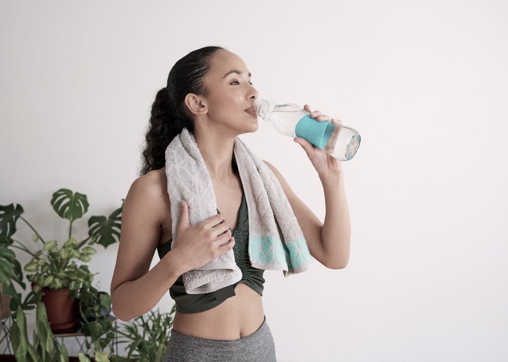 Woman sipping water while wiping off seat after a hot yoga session