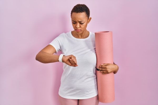 Woman holding a yoga mat looking at her watch