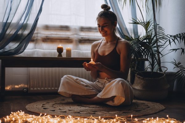 Woman holding a small candle in a dimly lit room while meditating