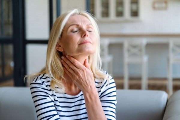 Senior woman holding her throat as a sign of blocked throat chakra