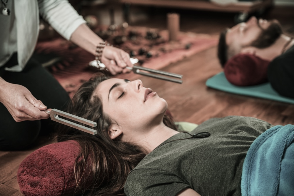 Woman lying on the floor while coach uses sound bath tools