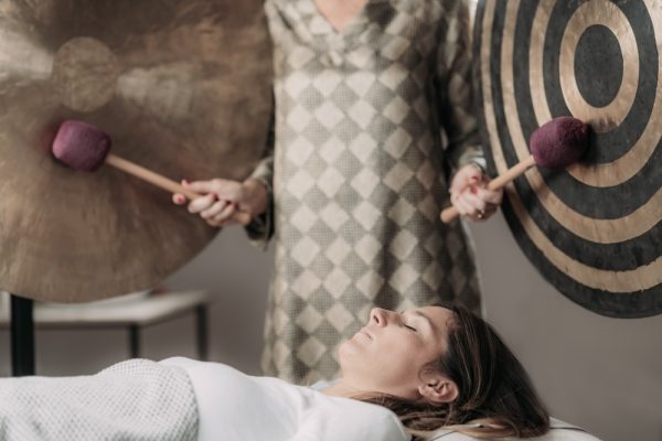 Woman in white clothing listening to sound of gongs behind her