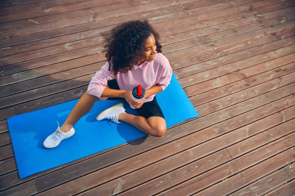 A woman sitting on a yoga mat, wearing yoga shoes while holding a white tumbler.