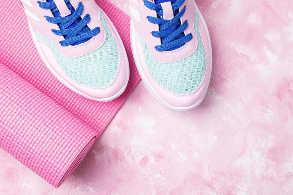 A pair of yoga shoes under a pink mat on a pink background.